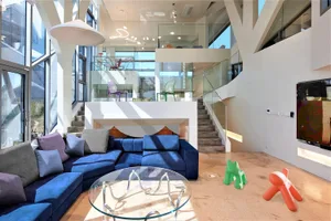 A modern living room featuring a blue sectional sofa, glass coffee table, and concrete structural elements.