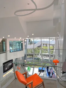 A modern living room with large glass windows, a glass table, and sleek metal accents.