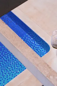Modern swimming pool exterior with blue tiled water and beige concrete deck.