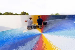 Two workers installing colorful mosaic tiles inside a swimming pool during renovation.