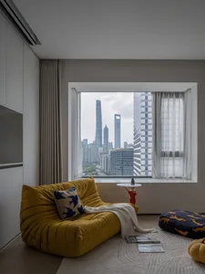 A minimalist interior featuring a yellow upholstered couch with blue bird-patterned cushions, viewed through a window showing