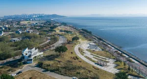 A modern coastal park with a curved pathway, greenery, and a building resembling sails.