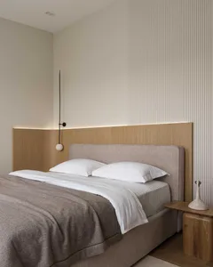 Minimalist bedroom with a wooden headboard, white bedding, and a side table with a white sculpture.