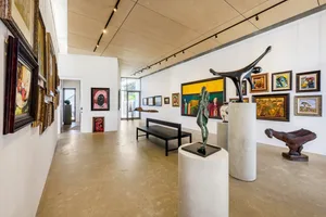 Modern art gallery with sculptures on concrete pedestals, metal figures, and paintings on the walls.