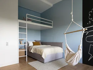 A modern bedroom with a gray bed and a hanging chair, featuring minimalist design and light blue walls.