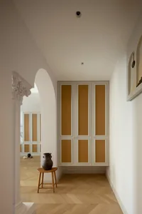 A modern hallway features wooden cabinets with woven accents, a wooden stool, and a decorative vase on top.