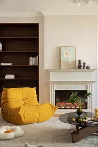 A spacious modern living room with a yellow upholstered armchair, a round glass coffee table, a white fireplace mantel with a