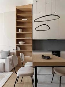 A modern minimalist kitchen featuring light-colored wooden shelves and a dining table with contemporary lighting fixtures.