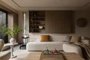A modern living room with a minimalist design, featuring neutral-toned furniture, a large window, a coffee table with magazin