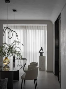 Modern dining room featuring a glass table with marble legs and timber chairs, white curtains, and minimalist decor.