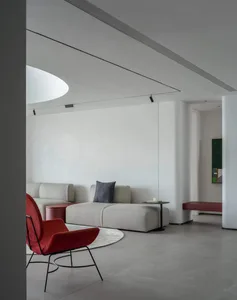 A minimalist living room featuring white walls, a modern sofa, and a single red accent chair.