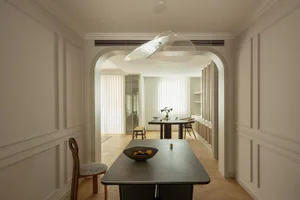 Modern dining room with wooden flooring, minimalist design, and a table with a bowl of fruits.