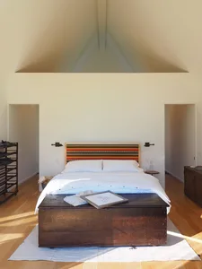 A minimalist bedroom featuring a wooden headboard and white linens on a large bed.