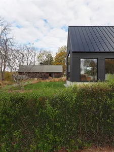 A modern house with a black-clad exterior featuring a metal roof and large windows.