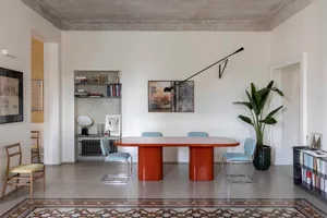 A modern dining room with a rectangular table featuring cylindrical concrete legs, surrounded by blue chairs and adorned with