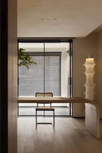 A minimalist home office featuring a wooden desk and chair in front of a window with blinds.