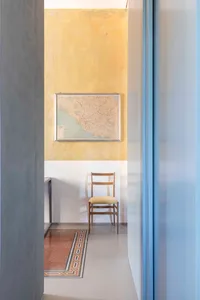 A modern home office with yellow painted walls, a map of Italy on the wall, a single wooden-framed cushioned chair, and a pat