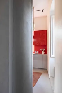Modern kitchen featuring red metal cabinets, white countertops, and a terrazzo floor.