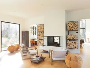A modern minimalist living room featuring a double-sided fireplace, floor-to-ceiling glass windows, and wood furniture.