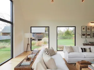 A modern living room with organic materials, featuring white sofas, a rustic coffee table, and large windows overlooking a gr