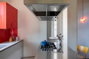 A modern minimalist kitchen with a white and red color scheme, featuring a sleek steel counter, a blue pot on a stove, and a 
