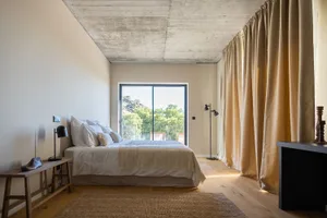 A minimalist bedroom with beige walls, a wooden floor, and a large bed with white bedding and pillows.