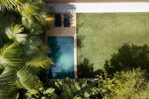 A minimalist outdoor living space featuring a wooden poolside patio with sun loungers and lush greenery surrounding a rectang