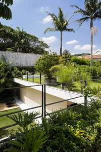 Modern minimalist backyard featuring a concrete bridge, wooden furniture, and metal railings surrounded by greenery and palm 