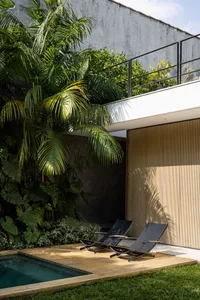 Modern poolside lounge area with concrete patio, wood deck, and lush green plants.