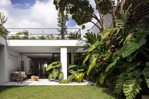 Contemporary white concrete residential exterior with lush green tropical plants and a minimalist balcony.