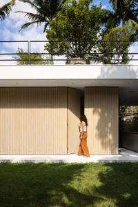A modern residential exterior with wood siding, large glass windows, and a lush green lawn.