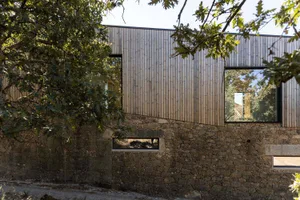 A modern house with a wooden exterior and stone foundation, framed by greenery.