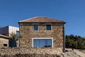 Rustic stone house with tiled roof and large windows.