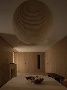 A minimalist interior space with wooden walls and furniture, featuring a large lamp and a bowl of objects on a table.