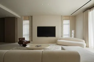 A minimalist living room with a neutral color palette featuring a sleek, curved sofa, a low wooden coffee table, a black flat