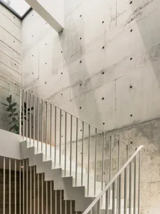 A minimalist staircase made of concrete, featuring white railings against a raw concrete wall.