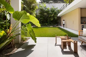 A modern balcony with concrete flooring, wooden furniture, and lush greenery.
