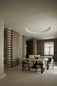 A modern minimalist kitchen with a circular dining table, wooden cabinets, and porcelain floor tiles.