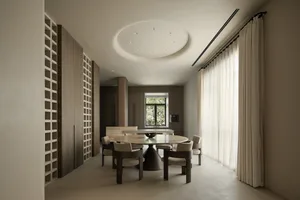 A modern residential dining room featuring a circular wooden table with marble top and matching chairs, surrounded by large w
