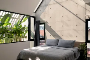 A minimalist bedroom featuring concrete walls and large windows with green plants.