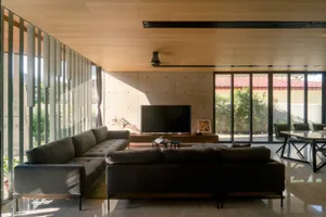 A minimalist living room featuring concrete walls and furniture, with large windows providing natural light.