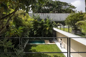 A person walking towards a modern minimalist house with a concrete and glass exterior surrounded by greenery.