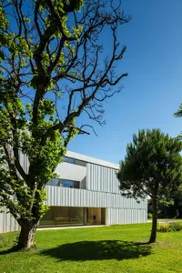 A minimalist residential building with a metal-cladding exterior on a sunny day with green trees in the foreground.