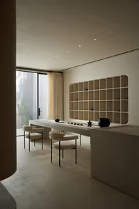 A minimalist interior space featuring concrete furniture and flooring, with a modern bookshelf and seating area by a large wi
