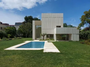 A modern house with a concrete facade and a swimming pool in the backyard with green grass.