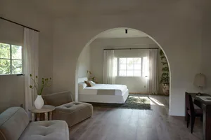 A minimalist bedroom with white furniture and soft lighting.