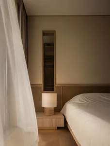 A minimalist bedroom featuring a wooden nightstand with a soft textile lampshade.