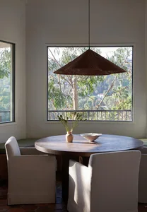 A modern dining room featuring a wooden table and chairs, with a pendant light hanging above and a view of trees outside thro