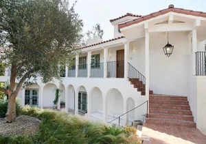 Stucco and terracotta exterior of a renovated Spanish-style home with white arches and terracotta roof tiles.