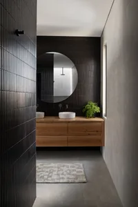 Minimalist bathroom with a black tiled wall, concrete flooring, and a wooden countertop featuring two sinks and a green plant